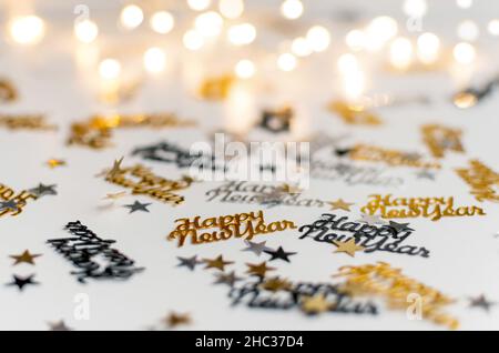 Selective focus photo of new year confetti sprinkled on white surface in front of bokeh lights Stock Photo