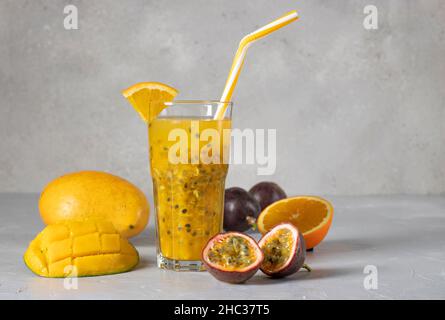 Tropical fresh of mango, passion fruit and orange in tall glass on gray background, Copy space Stock Photo