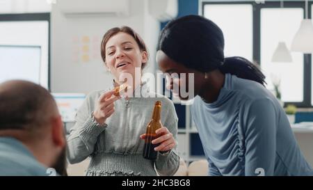 Group of colleagues having fun with drinks after work. Workmates enjoying bottles of beer and pizza while playing at foosball game table for entertainment. Coworkers after hours Stock Photo