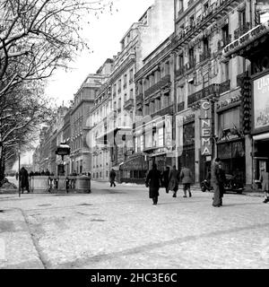 Paris Avenue des Champs-Elysees at Metro George V looking towards Arc de Triomphe in winter, 1945. One of two photographs that depict people walking and the businesses around the Metro with snow on the ground. There are almost no vehicles in sight and the photos were taken when the Champs-Elysees still had tree-lined medians that narrowed the boulevard into better pedestrian scale. Many of the people out are in military uniform. Businesses depicted along the northeast side of the avenue include Café George V, the Normandie, Milady, Lord Byron, and the cinema. Trees are laden with snow. Stock Photo