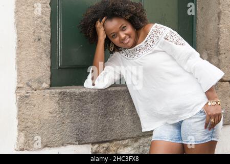 Model in a white dress smiling, looking and posing at the camera. In the background, the historical center of Pelourinho with its ancient architecture Stock Photo