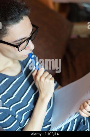 young man sitting on the sofa thinking what to write in his copybook Stock Photo