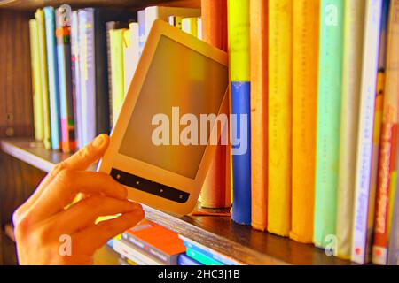 Electronic book picked from a library shelf. The electronic book on a bookshelf among the many books in the library. Booksand library concept Stock Photo
