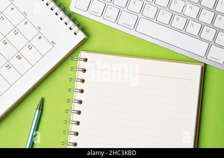 Open blank diary and desk calendar with computer keyboard on green background. Stock Photo