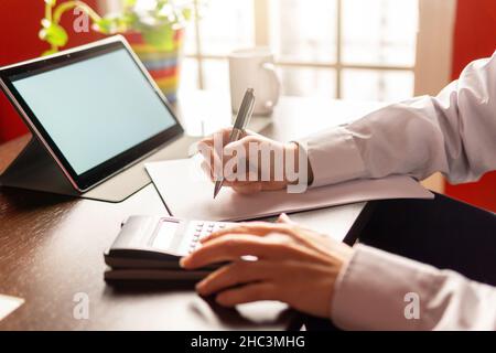 Woman writing and using a calculator, using digital tablet, businesswoman or student. Working from home concept Stock Photo