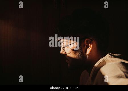 Side profile of a young handsome Hispanic man with glasses posing under the sunlight of golden hour Stock Photo