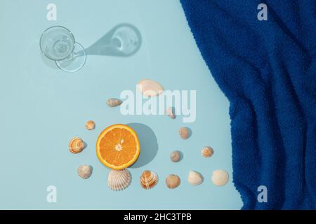Summer scene with dark blue beach towel and glass and orange fruit and shell. Minimal aesthetic. Stock Photo