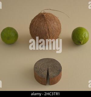 Coconut and two limes on beige background with a piece of wood . Minimal concept. Stock Photo