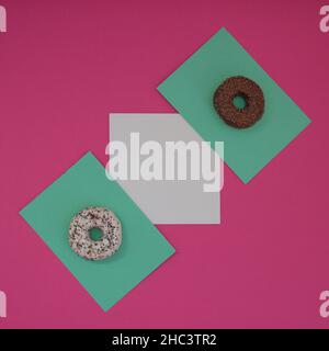 Two donuts sprinkled with chocolate crumbs on a light green surface, with white copy space, all on a pink background. Minimal flat flay composition. Stock Photo