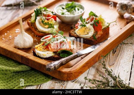 Appetizing canapes or sandwiches with smoked salmon. Toast with fish, soft cheese, eggs, onion rings and salad. Delicious breakfast or snack Stock Photo