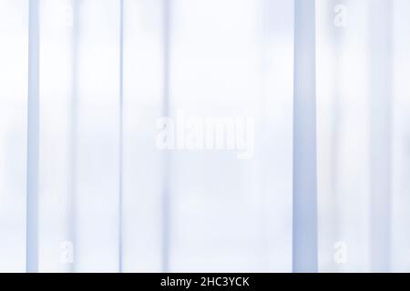 Light coming through a sheer, transparent and pleated light blue curtains or drapes. Striped, vertical linear patterns. Abstract soft background. Stock Photo