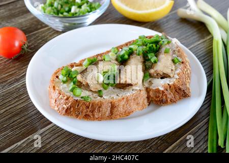 Sandwiches with smoked sprat, butter and green onions on the wooden background. Danish cuisine. Close-up. Stock Photo