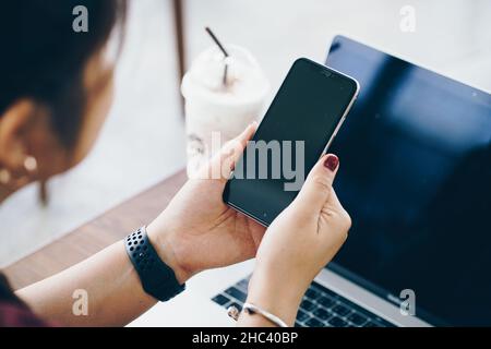 Mockup image of woman hand using black mobile phone with laptop screen while drinking coffee in cafe Stock Photo
