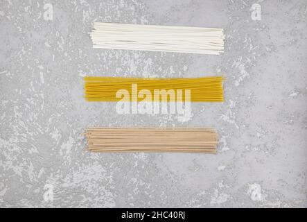 three types of dry Italian paste on a gray concrete background. noodles, spaghetti, buckwheat noodles. top view Stock Photo
