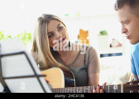 Woman teaching man how to play on guitar instrument, music class at home Stock Photo
