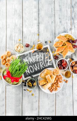 Happy Nowruz holiday background. Celebrating Nowruz sweets and treats- baklava, various dried fruits,  nuts, seeds, wooden background with green grass Stock Photo