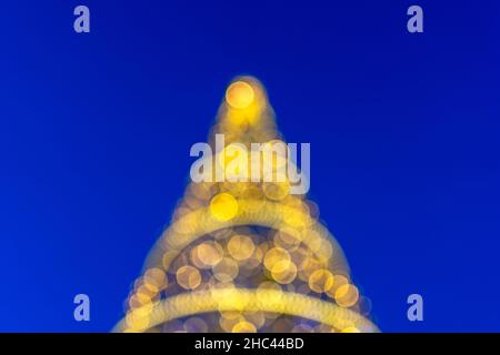 Blurred bokeh of Christmas tree with fairy lights on blue background. Stock Photo