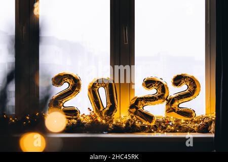 2022 golden foil balloons on blue window sill. Celebrating holidays at home, festive decor concept. Happy New Year 2022. close-up numbers of year 2022