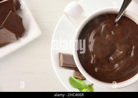 Hot chocolate detail in white ceramic cup on a plate with pieces of chocolate and mint leaves on white wooden table. Top view. Horizontal composition. Stock Photo