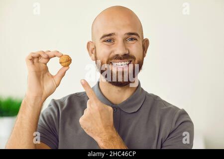 Portrait of confident man with beautiful healthy smile holding walnut in his hand. Stock Photo