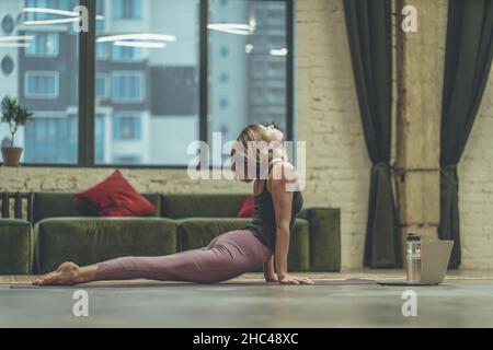 Young Woman Doing Yoga Asana Cobra on Yoga Mat on the Floor at Home. Home Workout, Strengthening the Back Muscles. Close-up. High quality photo Stock Photo