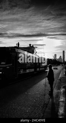 Vertical grayscale shot of an old man standing in the street as a tram passes. Stock Photo