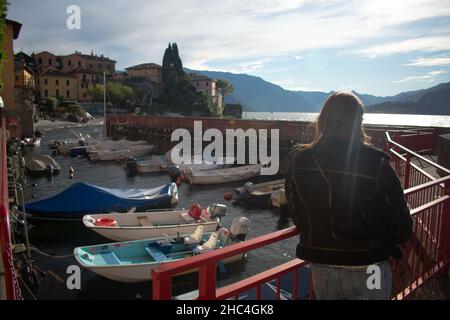 Female tourist overlooking quaint boat harbor outside of Varenna on Lake Como Italy Stock Photo