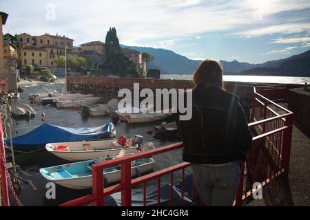 Female tourist overlooking quaint boat harbor outside of Varenna on Lake Como Italy Stock Photo