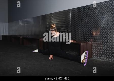 full length of young woman in white figure skates doing splits near wall Stock Photo