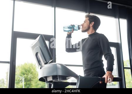 Side view of man drinking water on treadmill in sports center Stock Photo