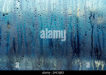 The transparent glass of the window is covered with dripping raindrops. The weather outside the window of the house. Background. Stock Photo