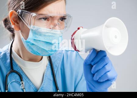 Female doctor yelling into megaphone microphone, agitated serious woman medic speaking to members of staff and medical colleagues in hospital or clini Stock Photo