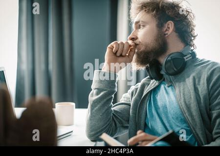 Pensive Man is Thinking How to Organize His Business Process During the Quarantine Period. A Man is Sad About His Problems in Life. Feet on the Table. Close-up. High quality photo Stock Photo