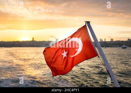 The Turkish Flag is waving in the wind against Istanbul Bosphorus at sunset. The flag of the Republic of Turkey. Stock Photo