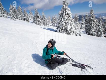 cheerful woman about 35 years old in winter clothes, helmet and skiing sits in the snow on a sunny winter day. a beginner skier has fun skiing on a sn Stock Photo