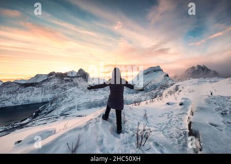 Back view of climber woman standing on snowy peak and mountain range view in the morning on mount Segla at Senja island, Norway Stock Photo