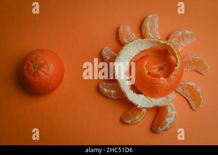 Organic mandarin wedges arranged in a circle with spiral peel and one whole mandarin on an orange paper background Stock Photo