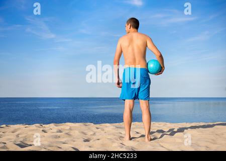 Young man with a volleyball on the beach. View from the back. Vacation concept. Stock Photo