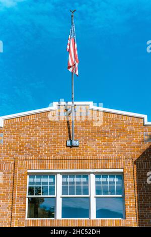 Vertical shot of an American Flag blowing on a brick wall building Stock Photo