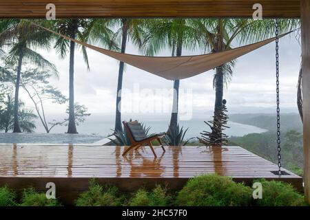 Empty chair on a wooden platform of a luxurious villa on a rainy day. Off-season vacation in Costa Rica. Stock Photo