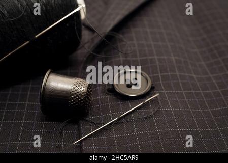 A needle and thread sews up a button on a plaid suit. Thimble. Textile Stock Photo