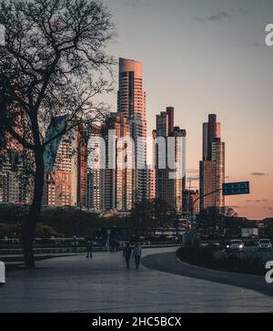 Vertical shot of a paved road and walking people with skyscrapers on the background at sunset Stock Photo