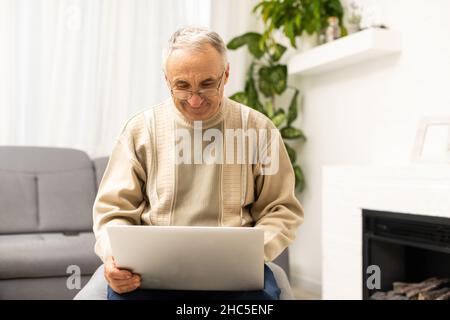 Elderly man with glasses using laptop at home Stock Photo