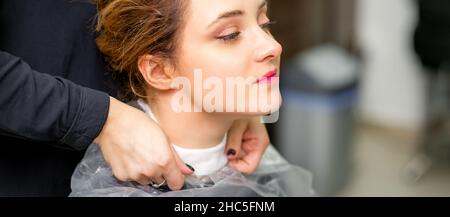 A hairdresser is covering a female neck with a cape for a female client in a beauty salon, close up Stock Photo