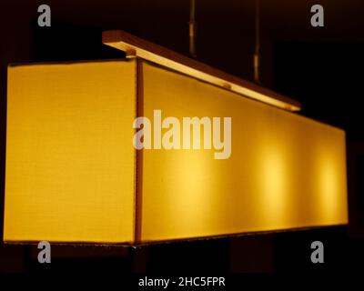 Lit modern lamp with a soft yellow light on a dark background Stock Photo
