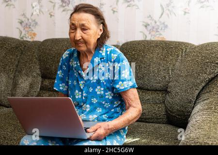 very old woman using laptop sitting in her sofa Stock Photo