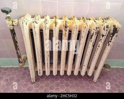 Old-fashioned home heating radiator in pink and green tiled bathroom Stock Photo