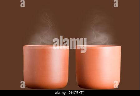 two ceramic clay cups with coffee or chocolate, isolated with brown background Stock Photo