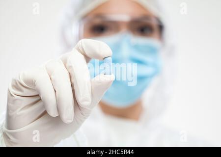 Female UK pharmacist wearing PPE personal protective equipment,coveralls,face mask,eyewear,glove,holding blue pill,selective focus,patient cure and re