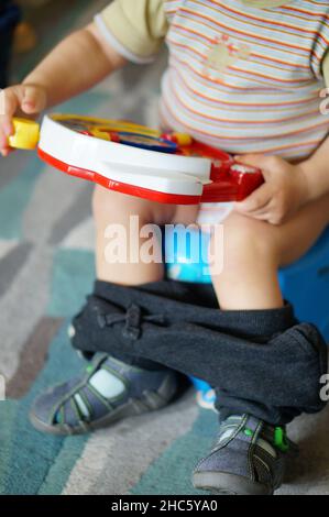 A young boy sitting on a potty while holding a farm sound toy Stock Photo